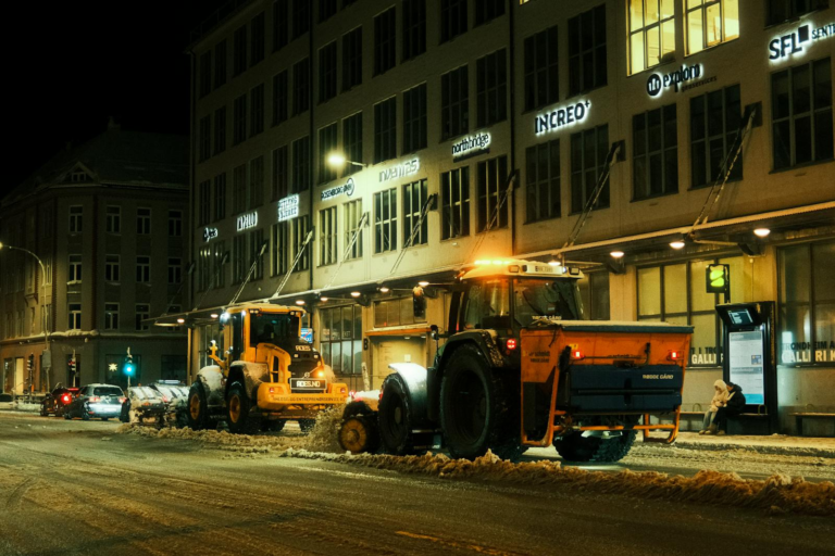 Snow plows clearing city streets at night, urban winter maintenance captured under streetlights.